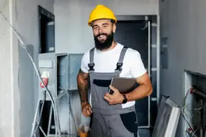 Electrician wearing a yellow hard hat, holding a clipboard, on site.